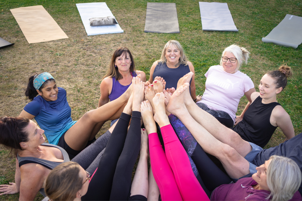 Students at a yoga class touching their toes together and smiling 